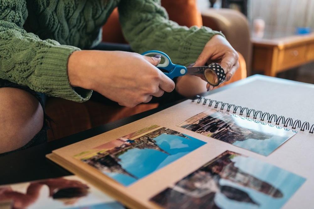 cutting a piece of washi tape to paste some photos into her handmade kraft travel paper album