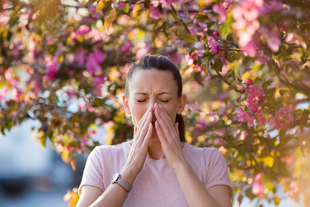 woman sneezing in front of blooming tree