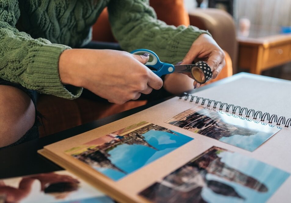 cutting a piece of washi tape to paste some photos into her handmade kraft travel paper album cutting a piece of washi tape to paste some photos into her handmade kraft travel paper album