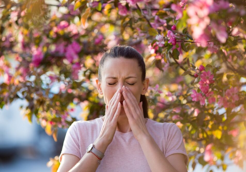 woman sneezing in front of blooming tree woman sneezing in front of blooming tree