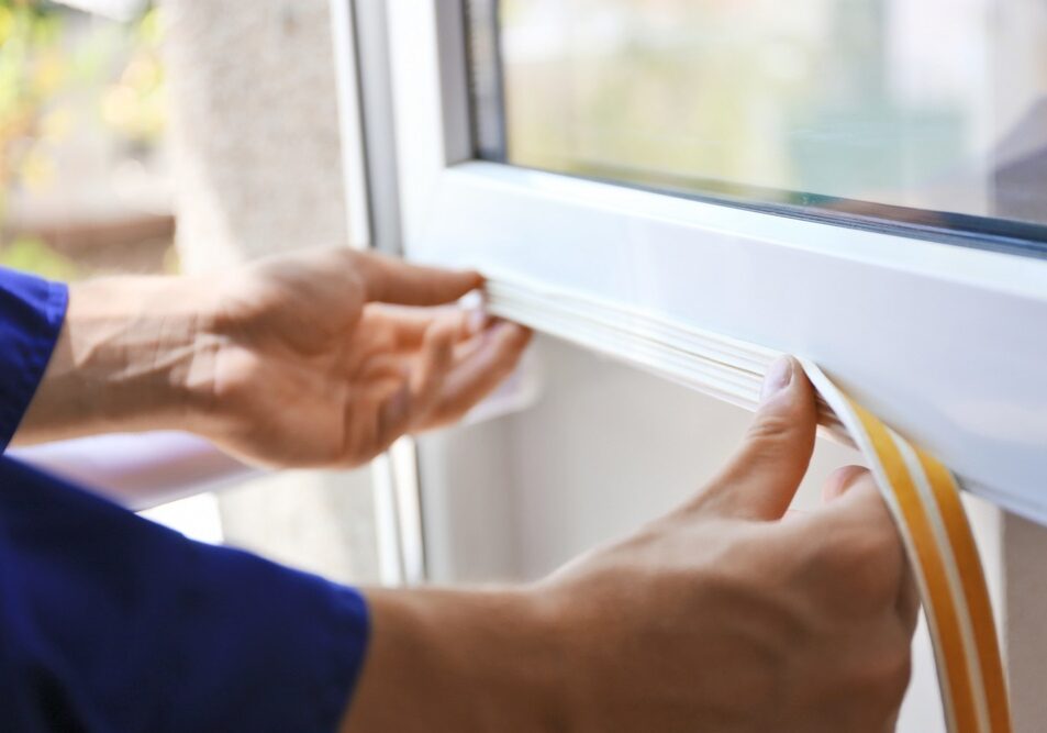 Construction worker putting sealing foam tape on window in house Construction worker putting sealing foam tape on window in house